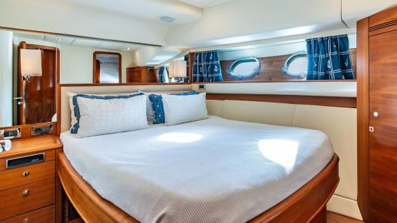 The cabin of Parodia II in Mallorca includes a centrally placed bed two windows with blue curtains and lighting.