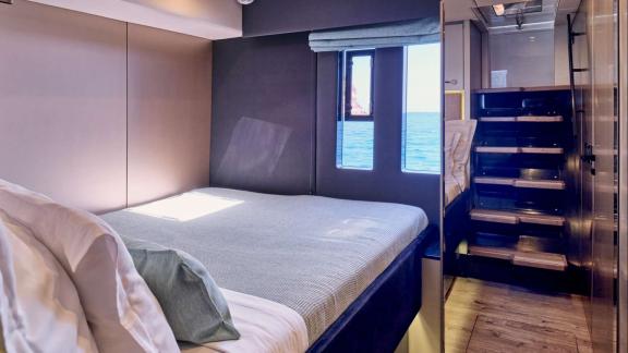 Modern cabin with a large bed, sea view windows, and stairs leading to the upper deck.