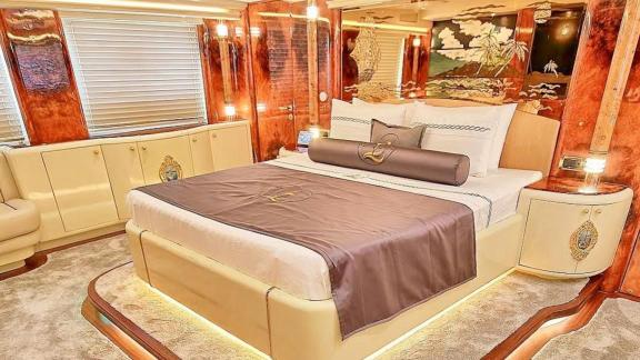 Роскошная кровать стоит на пьедестале с ковровым покрытием в окружении ценных пород дерева и точечных светильников.