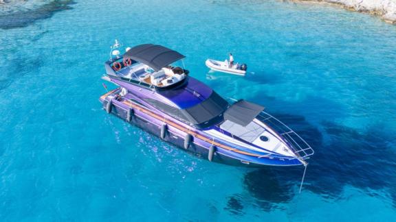 Die Motoryacht Karan liegt vor Anker im türkisfarbenen Wasser mit einem Boot im Hintergrund.