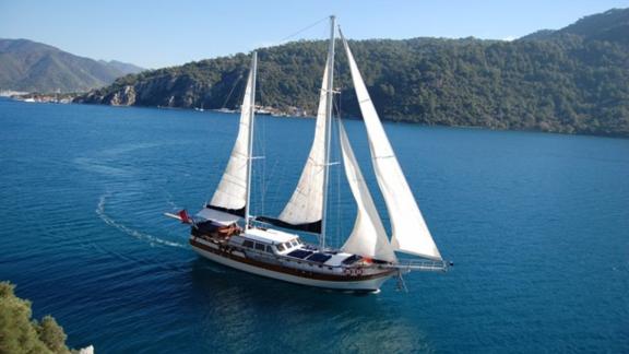 Gulet Remzi Yılmaz sails through the turquoise waters of Marmaris, surrounded by green hills and beautiful coastline.