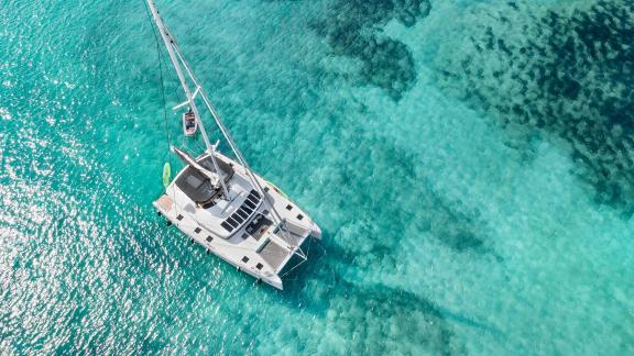 Aerial view of a Lagoon catamaran sailing or anchored in brilliantly clear, turquoise waters.