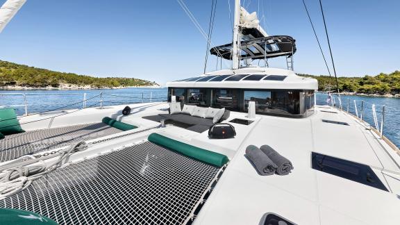 Front deck of a Lagoon catamaran featuring nets, sun loungers, and towels, surrounded by calm waters.