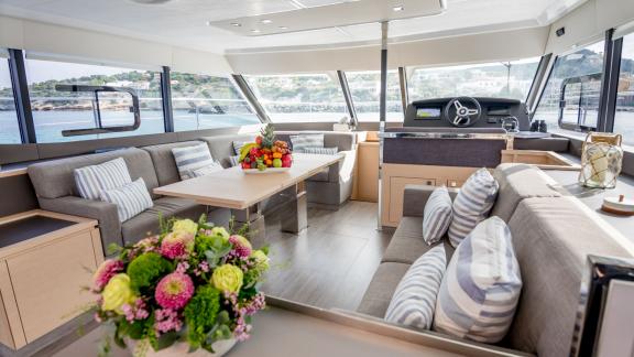 Cozy living area of a modern catamaran with large windows and a dining table adorned with fresh flowers.