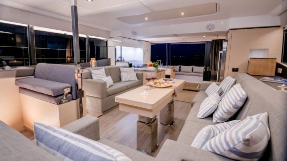 Stylishly furnished living area of a catamaran, illuminated at night, featuring cozy sofas and a set dining table.