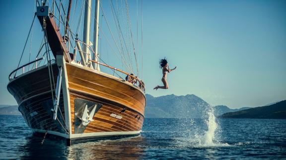 A person jumps from the gulet Entre Cielos into the blue sea off the coast of Athens, surrounded by clear skies and moun