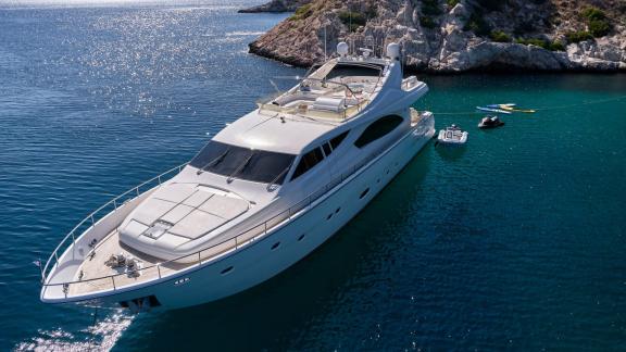 A sleek motor yacht anchored in clear blue waters against a rocky coastal backdrop.