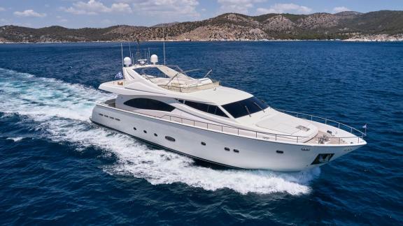 A sleek motor yacht glides over the blue sea with scenic mountains in the background.