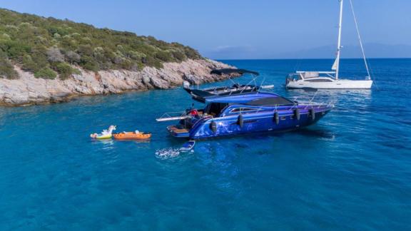 Karan motor yacht anchored near a rocky shore, with guests swimming and kayaking in the sea.