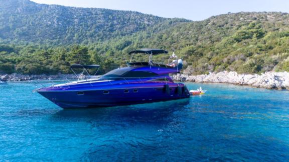 Die Motoryacht Karan liegt vor Anker in türkisfarbenem Wasser mit grüner Natur und Bergen im Hintergrund.