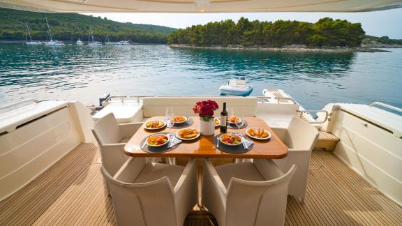 Ferretti 681 Dominique features an aft deck with a dining table and comfortable seating overlooking the water.