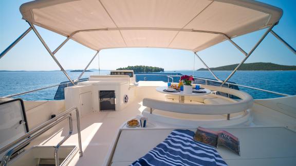 Ferretti 681 Dominique features a shaded flybridge with lounge seating and a table overlooking the sea.