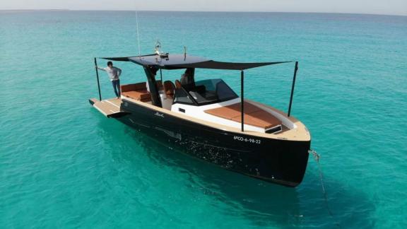 Ibiza'da demirlemiş Martone motoryatın gölgelikli ön güverte alanı ve yan güvertede duran bir kişi görülüyor.