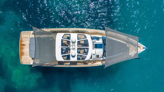 Vor der Küste Mallorcas liegt die Motoryacht Petitchet mit geöffneten Sonnensegeln in türkisfarbenem Wasser vor Anker.