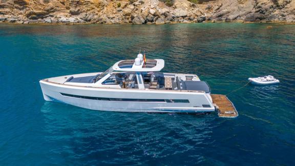 Vor der Küste Mallorcas liegt die Motoryacht Petitchet ruhig vor Anker, mit einem kleinen Beiboot am Heck.