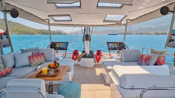 Cozy lounge area with cushions and drinks on the aft deck of the catamaran, surrounded by sea and hills.