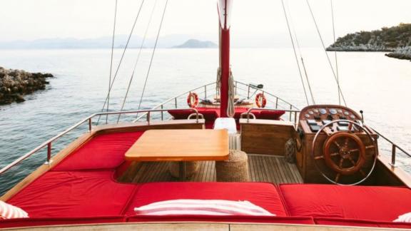 Red deck with helm and seating area on a yacht overlooking the calm sea.