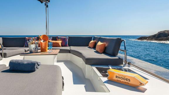 Seating area on a catamaran, decorated with cushions and a sign, overlooking the open sea.