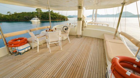 Deck of the gulet Vega with dining table and seating, surrounded by calm water and other boats in the background.