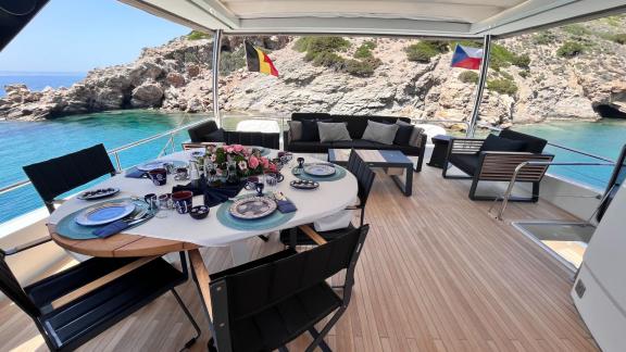 A beautifully set dining table on a luxurious catamaran, offering stunning views of the rocky coastline and clear waters