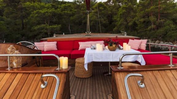 Inviting seating area with a set table and candlelight on a yacht, surrounded by forest.