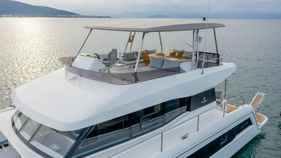 A spacious flybridge with seating area and helm on a modern catamaran gliding over calm waters.