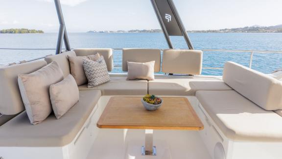 The Power 67 Ariva features a flybridge lounge with soft cushions and a wooden table overlooking Corfu bay.