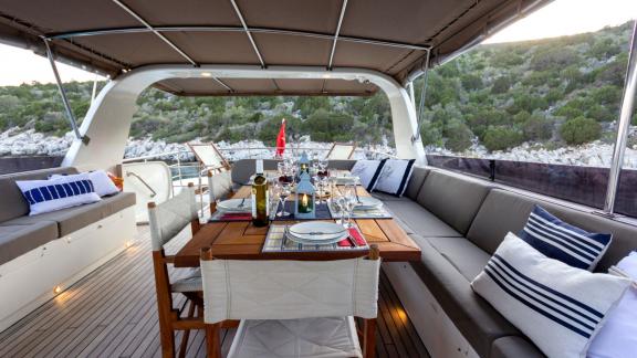 The upper deck of Sveti Sky features a wooden dining table, spacious sofas and a coastal view.