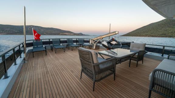 Comfortable seating area on the spacious aft deck of the yacht with a sea view and a waving Turkish flag.