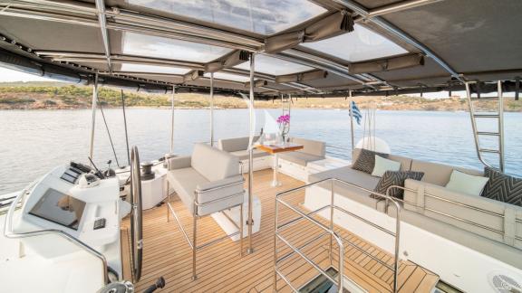 Spacious flybridge with seating, dining table, and helm station, overlooking the sea and coastline.