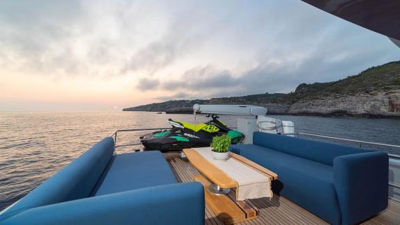 The upper deck of Stela 117 features a cozy seating area with sunset views and a jet ski in sight.