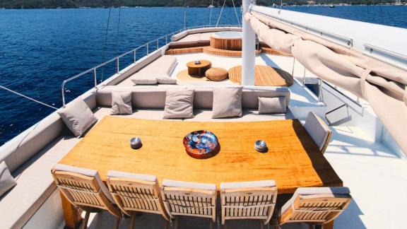 A dining table on the deck of a gulet with seating and a whirlpool in the background.