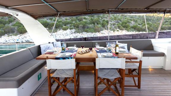 The flybridge of Sveti Sky features a wooden dining table surrounded by spacious seating areas.