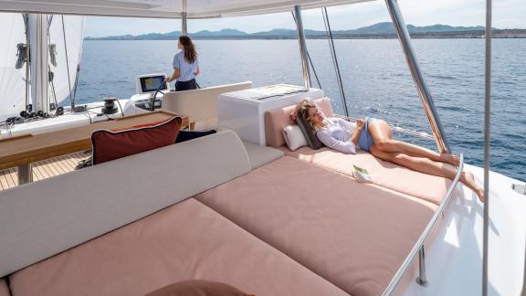 One person relaxes on a sunbed while the catamaran sails smoothly through calm waters.