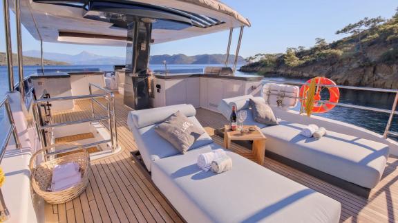 The flybridge features a relaxation area with comfortable sun loungers and a drinks table.