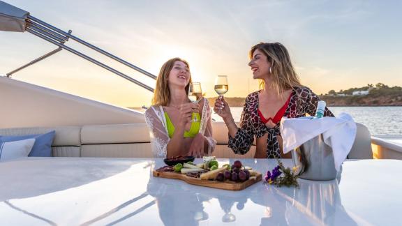 Zwei Frauen genießen Wein bei Sonnenuntergang auf der Yacht Pareaki, mit einer atemberaubenden Aussicht.