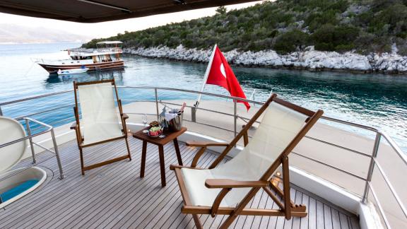The upper deck of Sveti Sky features two sun loungers, a small table and a turquoise bay in the background.