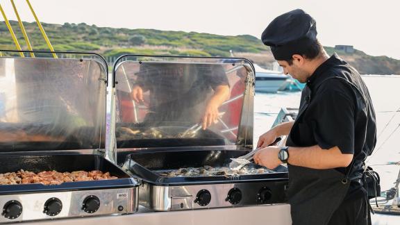 Chef grilling fresh food on board during a Greece day tour from Athens by catamaran.