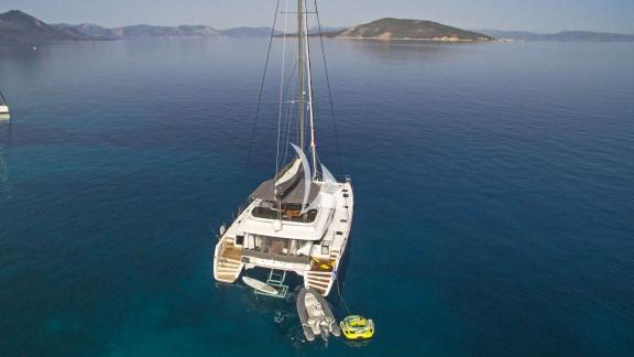 For Sail catamaran anchored in clear blue waters, with a tender and water sports equipment at the stern.