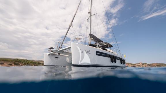 Side view of Lagoon For Sail 560 S2 catamaran in clear water with coast and sky in the background.