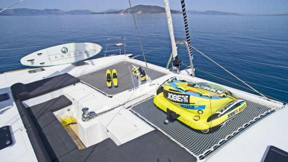 Net area with paddleboard, fins, and inflatable water toy on the front deck of a catamaran.