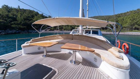 The deck of a Bodrum gulet with 5 cabins, equipped with comfortable seating and wooden tables, against a picturesque coa