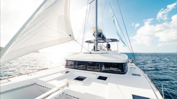 Akana sails in open sea with front deck view and sails full in bright sunlight.