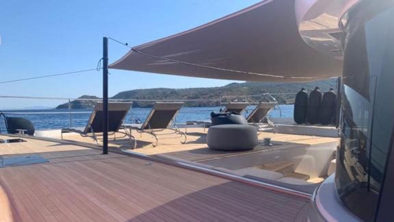 A shaded sun deck on a luxurious catamaran, equipped with sun loungers, offers a stunning view of the coastline in Greec