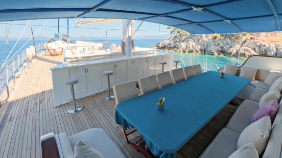 The covered dining area on the deck of the gulet Tarkan 5 in Fethiye, with a large table, bar stools and comfortable sea