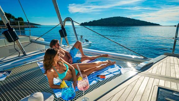 Guests enjoying the sun and cool drinks on the net of the catamaran Amada Mia in Croatia