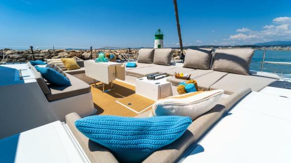 The lounge area of the Bali 5.4 catamaran invites you to relax under the Italian sun with views of a lighthouse.