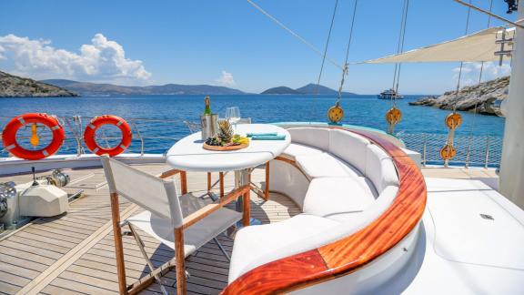 The aft deck of the Gazella gulet features a round table and a comfortable seating area. The table is set with tropical