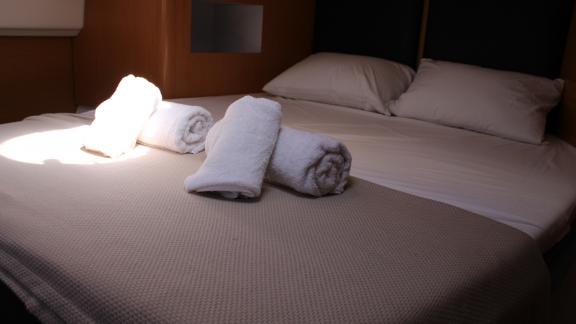 Double bed with folded white towels on the blanket in a cabin of Catamaran Ayda1.