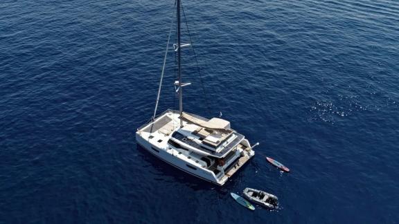 Helidoni charter catamaran anchored with tender and paddleboards in deep blue sea.